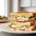 photorealistic chicken avocado melt sandwich on plate with melted cheese and avocado layers