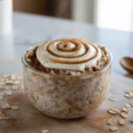 bowl of cinnamon roll overnight oats topped with cream cheese drizzle and cinnamon in bright modern kitchen