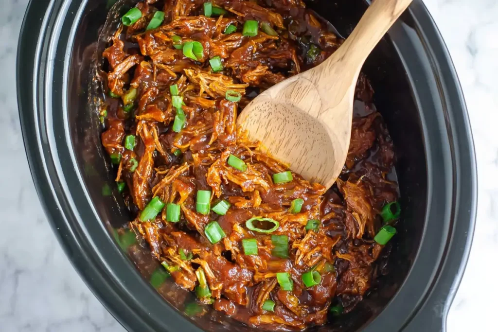 Slow Cooker Honey Garlic Chicken finishing in the crockpot with thick sauce green onions and sesame seeds