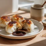 photorealistic close-up of Yaki Onigiri grilled rice balls on a plate in a modern kitchen, showing crispy golden crust and steam