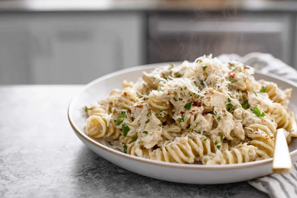Mixing rotini pasta into crockpot garlic parmesan chicken pasta in a modern kitchen