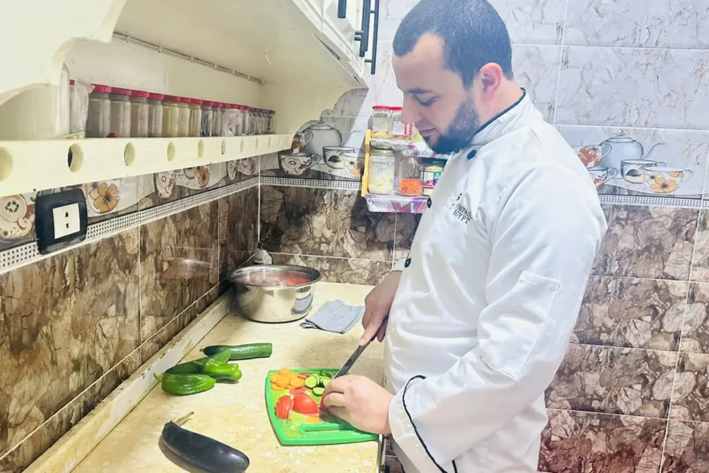 About 2 Chef Taha Ayad slicing fresh vegetables on a cutting board, preparing a recipe in his home kitchen