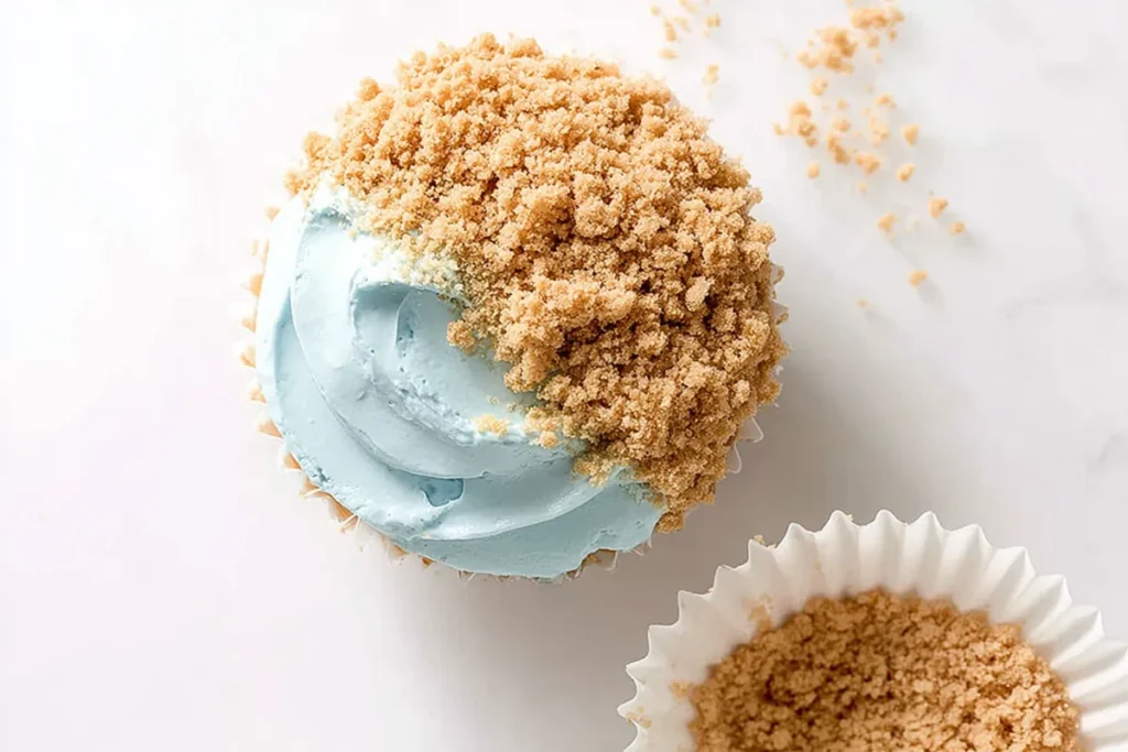 Beach cupcakes being topped with graham cracker sand over white frosting