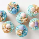 Chef Taha Ayad's Recipe Beach Cupcakes decorated with blue frosting, graham cracker sand, and candy seashells