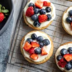 Chef Taha Ayad's Recipe Mini Fruit Pizzas with cream cheese frosting, strawberries, and blueberries on a cooling rack