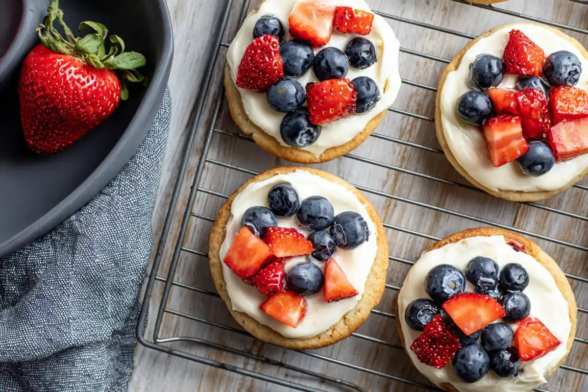 Chef Taha Ayad's Recipe Mini Fruit Pizzas with cream cheese frosting, strawberries, and blueberries on a cooling rack