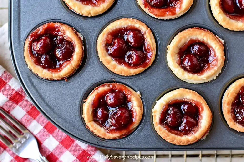 Mini Cherry Tarts with Cream Cheese Crust (Easy Homemade Version) 8 Mini Cherry Tarts baking in a muffin pan with glossy cherry filling and golden cream cheese crust
