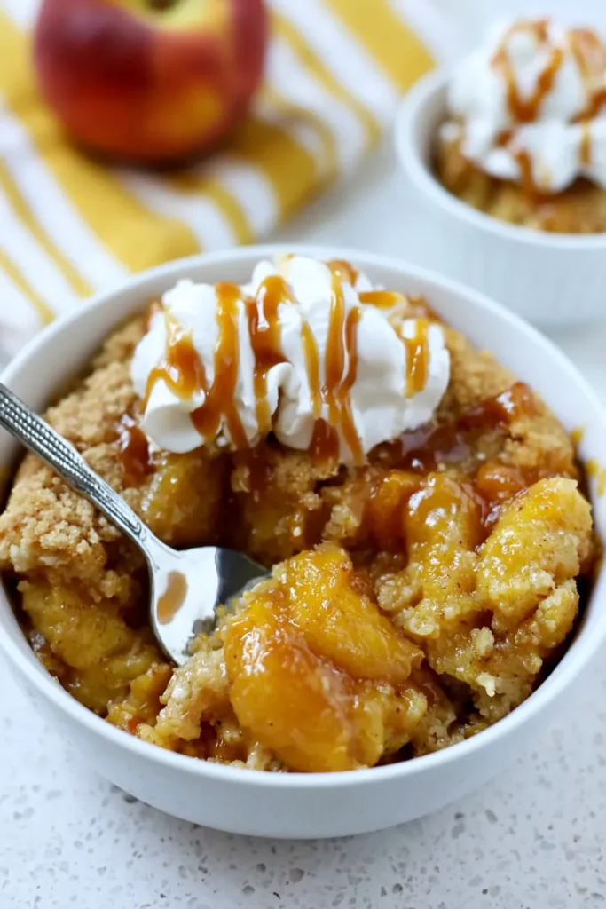Peach Dump Cake recipe served in a bowl with whipped cream and caramel drizzle