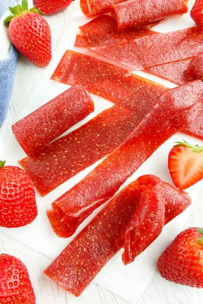 Strawberry Fruit Roll-Ups with Just 3 Simple Ingredients 2 Homemade Strawberry Fruit Roll-Ups cut into chewy strips with fresh strawberries