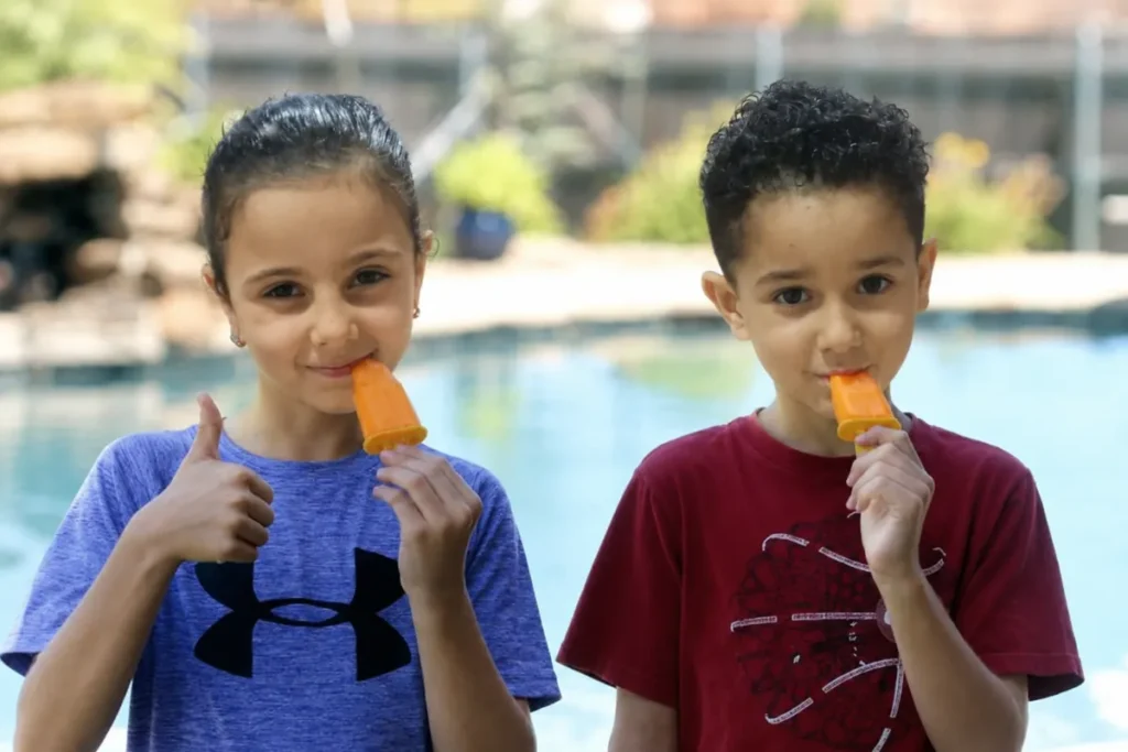 Easy Jell-O Popsicles That Hold Their Shape Longer 5 Two orange Jell-O Popsicles in small reusable molds near a sunny kitchen window
